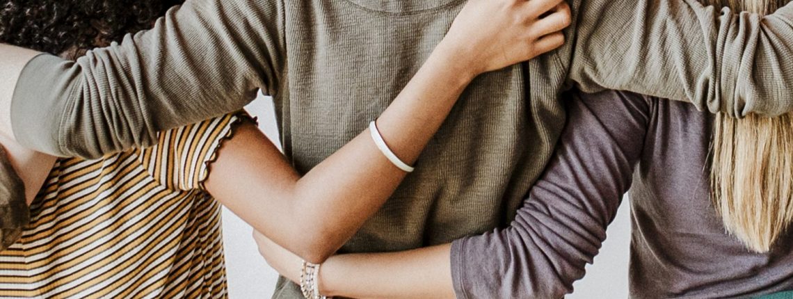 View from behind of four people with their arms around one another's shoulders