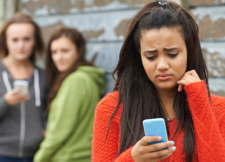 Teen girl looking at cell phone with two teen girls behind her