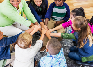 Teacher and students with their hands in a circle