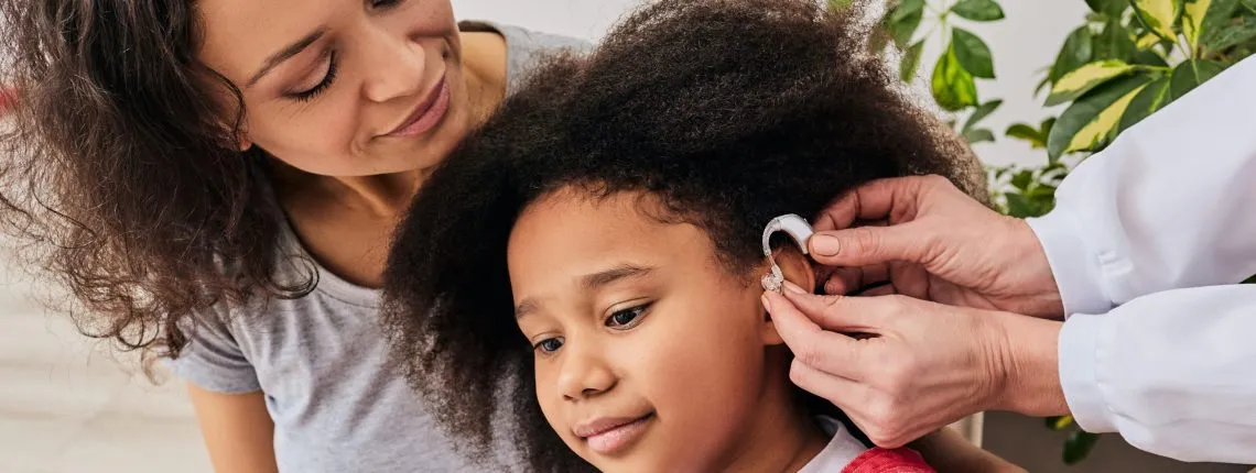Hearing treatment for a child. African American girl with her mother during installation hearing aid by her audiologist