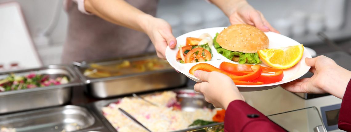Pleasant woman giving lunch to school girl in cafeteria